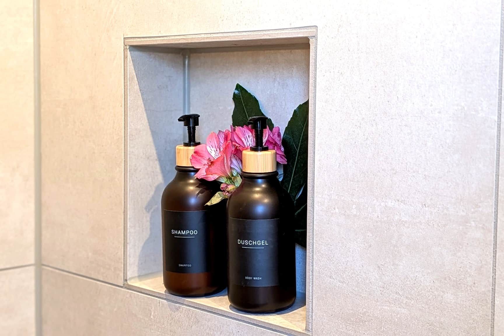 Zwei Shampoo- und Duschgelflaschen auf einem Ablagebrett im Badezimmer.