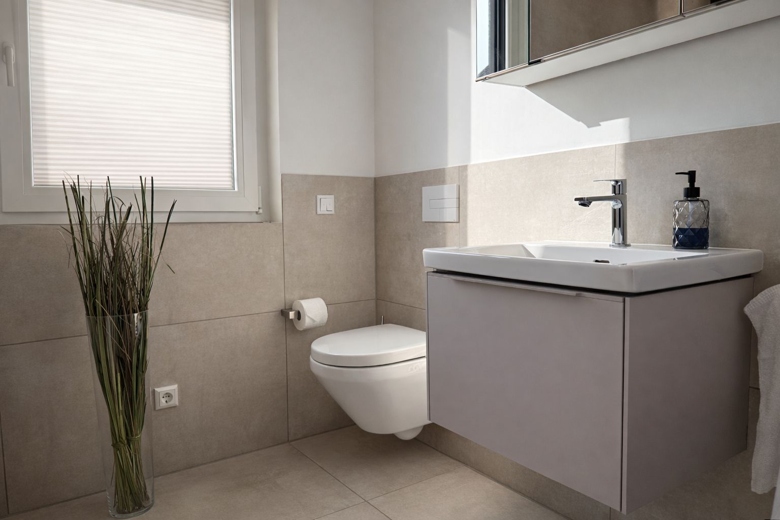 Een badkamer met toilet, wastafel en een hoge vaas met planten.
