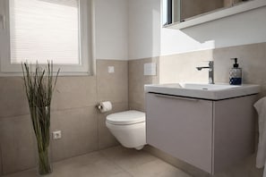 Un baño con inodoro, lavamanos y un jarrón alto con plantas.