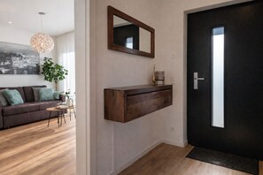 Una sala moderna con una puerta oscura, un espejo montado y una consola de madera.