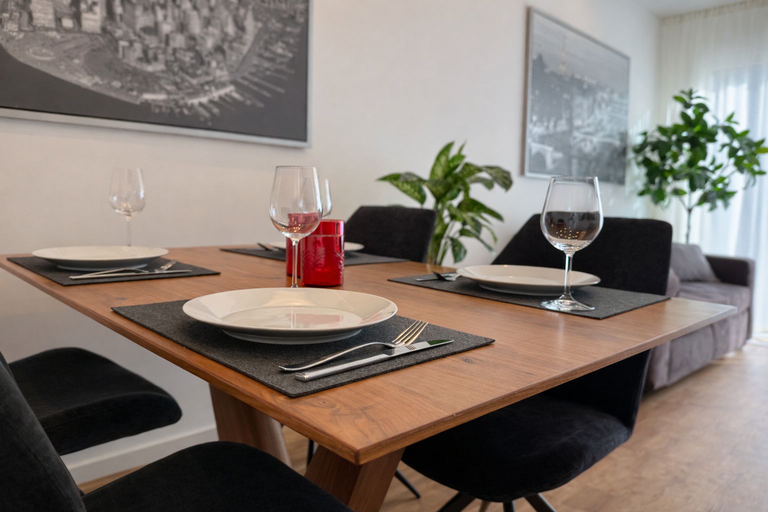 Een eettafel gedekt met borden, bestek en wijnglazen, met een rode kaars en een plantje op de achtergrond.