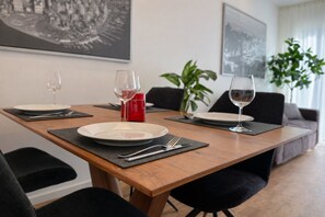 Una mesa de comedor dispuesta con platos, cubiertos y copas de vino, con una vela roja y una planta al fondo.