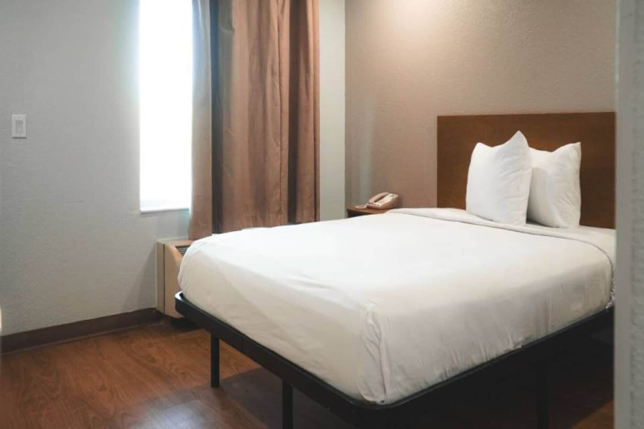 Quarto de hotel com cama, telefone ao lado e janela com cortinas.