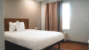 A hotel room with a bed, a bedside telephone, a window with curtains, and a radiator. - ADA Queen Bed|RI Shower|Nsmk|Kitchen (Rancho Cordova)