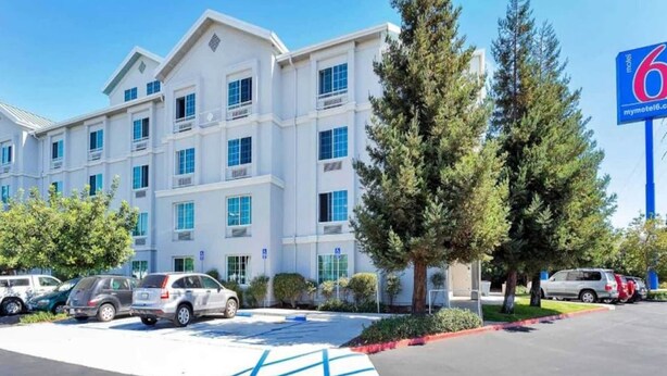 Un hotel de varios pisos con un estacionamiento, varios automóviles y un letrero del motel.