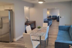 A modern kitchen with a stainless steel refrigerator, a dining table with chairs, and a blue sofa in the living area. - 1 Queen Bed | Premium, Mini Fridge (Las Vegas)