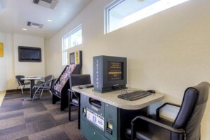 Ein kleiner Bürobereich mit einem Computer, einem Stuhl, einem Schreibtisch und einem an der Wand befestigten Fernseher.