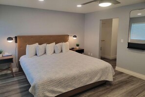 A bedroom with a large bed, a nightstand, a wall-mounted lamp, and a door leading to another room. - 1 Queen Bed | Premium, Mini Fridge (Las Vegas)