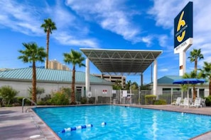 Ein Pool mit überdachtem Bereich, Palmen und einem Hotelschild.