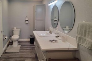 A bathroom with a toilet, sink, mirror, and a trash can. - 1 Queen Bed | Premium, Mini Fridge (Las Vegas)