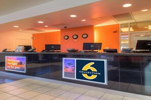 Een hotel receptie met een modern design, met een zwart receptiebalie, oranje muren en meerdere computermonitoren.
