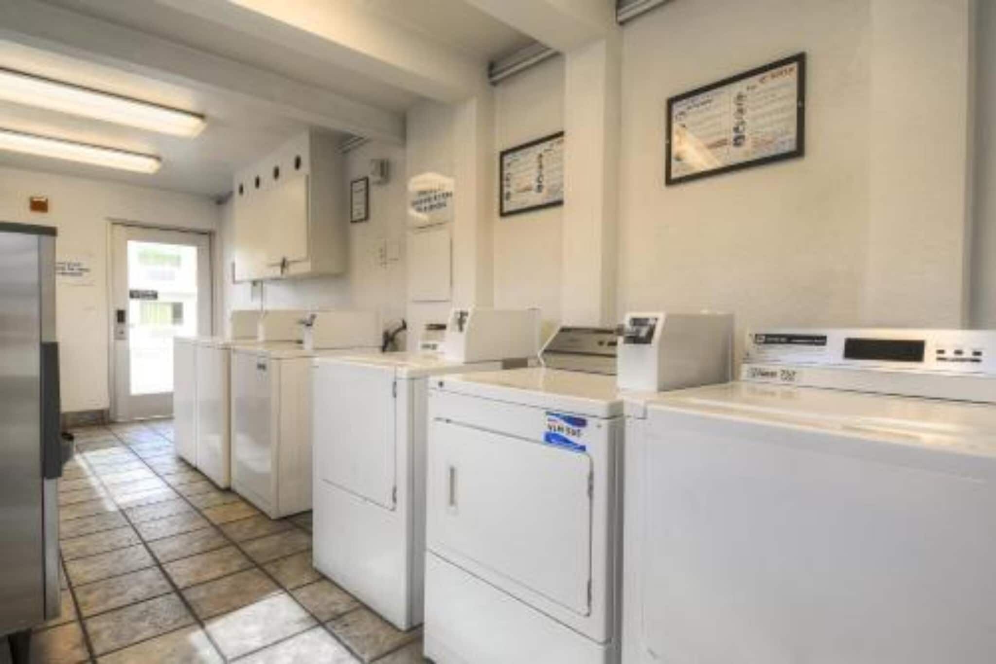 A laundry facility with multiple washing machines and dryers, a tiled floor, and a door leading outside.