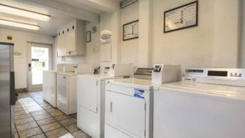 A laundry facility with multiple washing machines and dryers, a tiled floor, and a door leading outside.