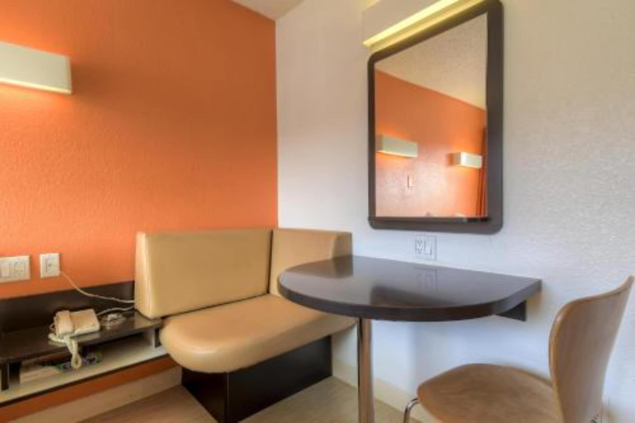 A hotel room with a sofa, a small table, a chair, and a mirror on the wall.