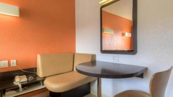 A hotel room with a sofa, a small table, a chair, and a mirror on the wall.