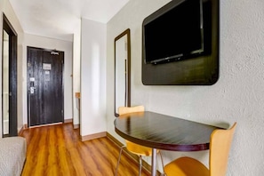 A room with a wooden floor, a dining table with chairs, a television mounted on the wall, and a door. - 2 Queen Beds | Non-Smoking, Micfridge (Moriarty)