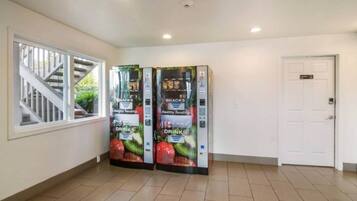 Un couloir avec deux distributeurs automatiques, dont l’un est étiqueté « Distributeur de produits sains » et l’autre « Encas », une porte blanche et une fenêtre donnant sur un escalier.