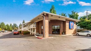 Un motel con una estructura de un solo piso, una zona de estacionamiento techada y un cielo azul despejado.