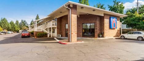 A motel with a single-story structure, a covered parking area, and a clear blue sky.