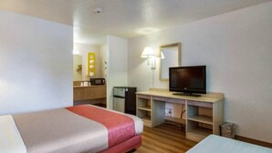 Habitación de hotel con dos camas, un escritorio con televisor, una kitchenette pequeña y un espejo.