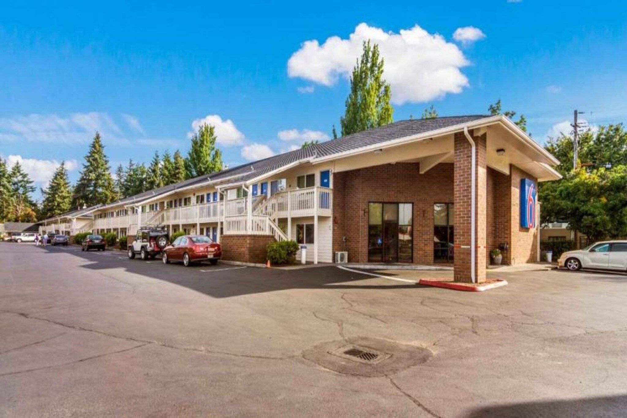 Et motel med murstensfacade, flere balkoner og en parkeringsplads.