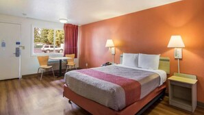 Habitación de hotel con una cama, dos lámparas de noche, un escritorio con una silla y una ventana con vista a un coche estacionado afuera.