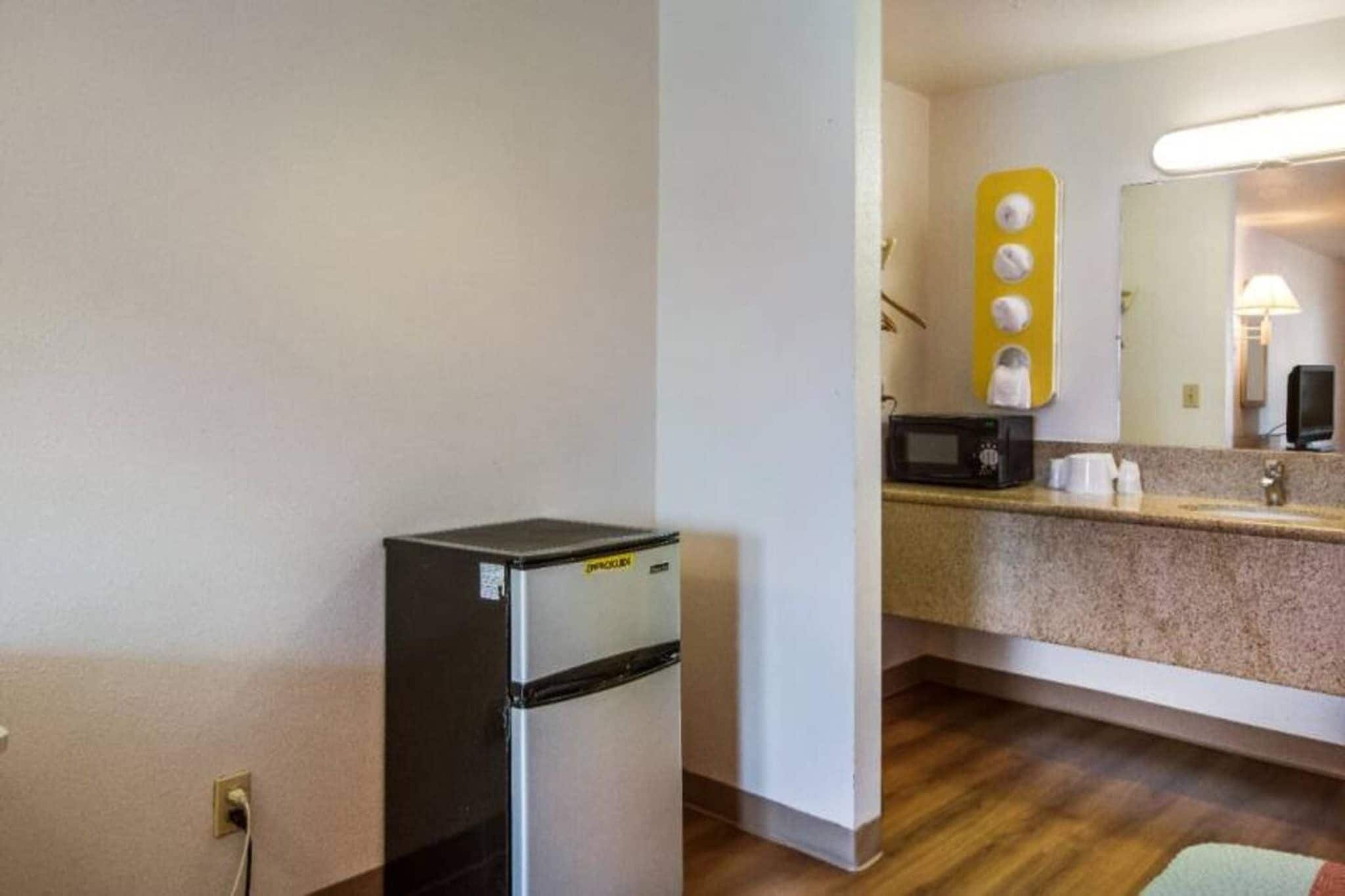 Une petite cuisine équipée comprenant un réfrigérateur, un four à micro-ondes et un petit plan de travail agrémenté d’un miroir et d’un luminaire jaune.