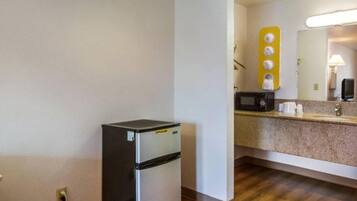 Une petite cuisine équipée comprenant un réfrigérateur, un four à micro-ondes et un petit plan de travail agrémenté d’un miroir et d’un luminaire jaune.