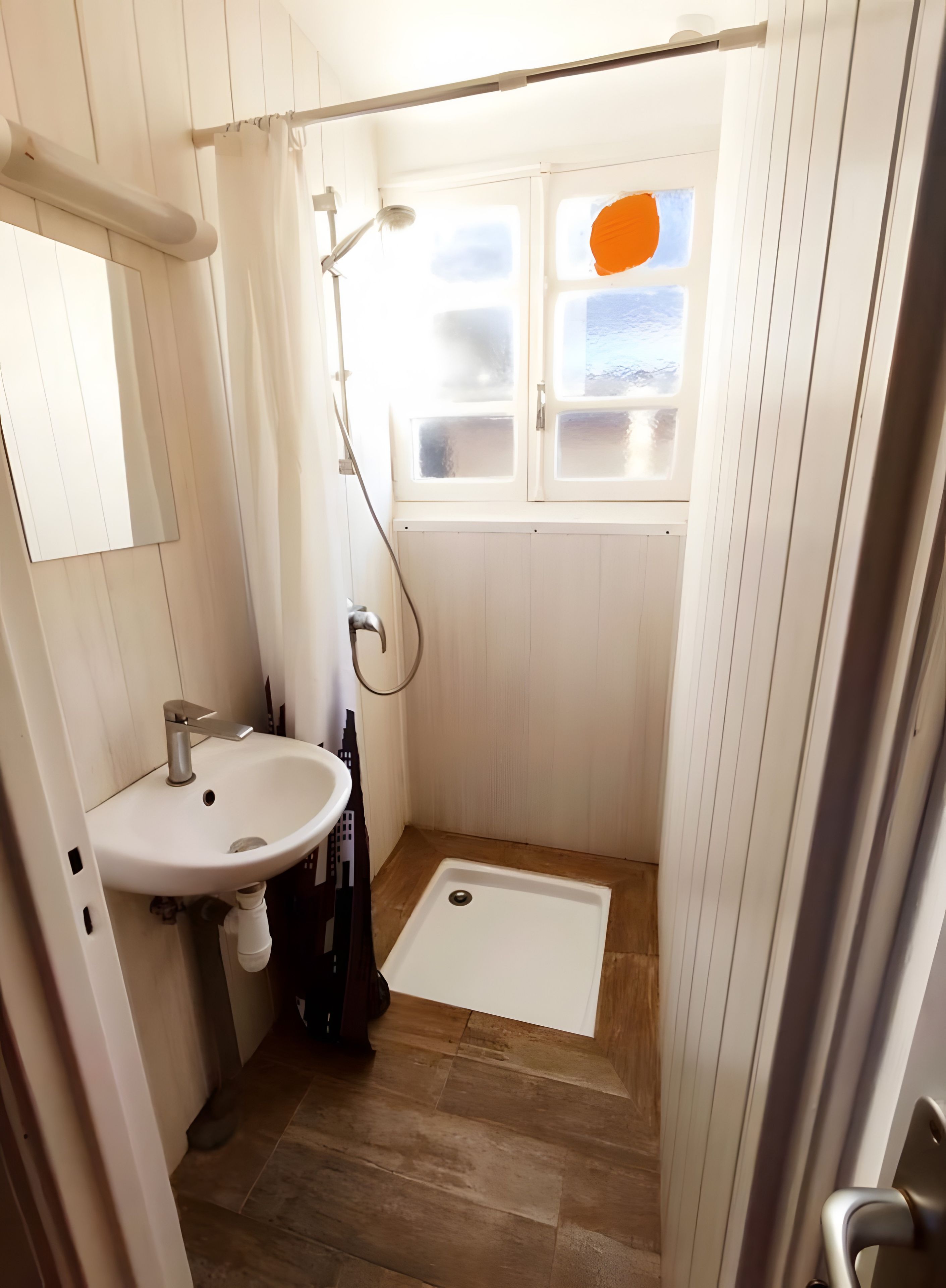 Un bagno con doccia, lavandino e finestra con vetri satinati.