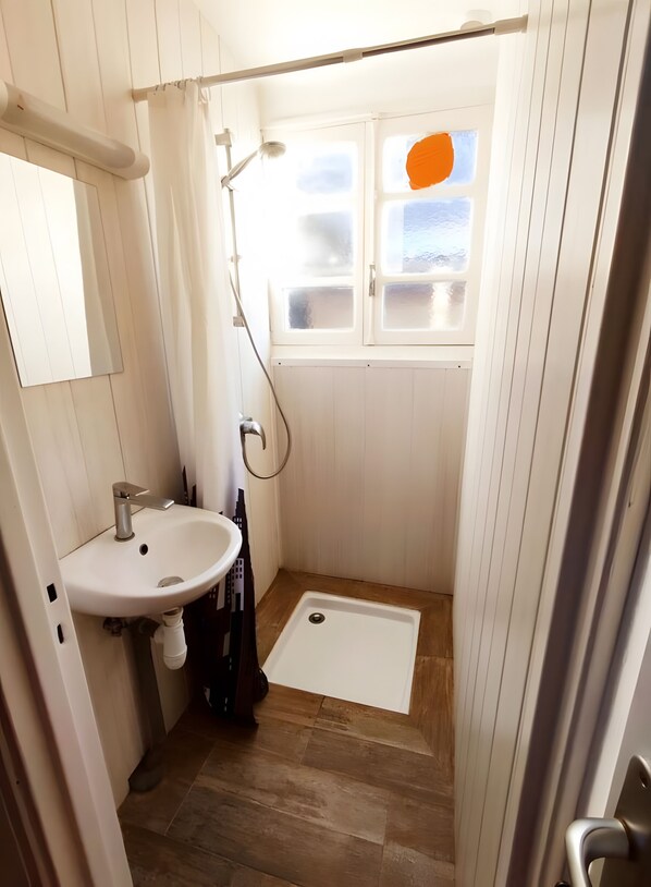Een badkamer met een douche, wastafel en een raam met gezandstraalde panelen.