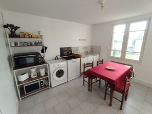 A compact kitchen with a washing machine, microwave, and a dining area with a table and chairs.