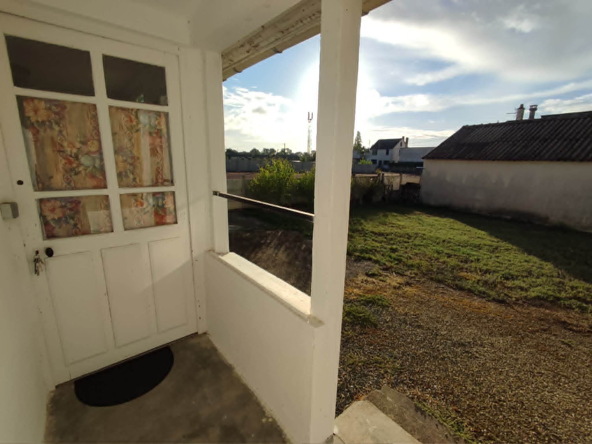 A white door with a window, a small porch area, and a view of a grassy yard with houses in the background.