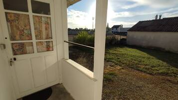 A white door with a window, a small porch area, and a view of a grassy yard with houses in the background.