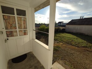 Una porta bianca con una finestra, un piccolo portico e vista su un prato con case sullo sfondo.