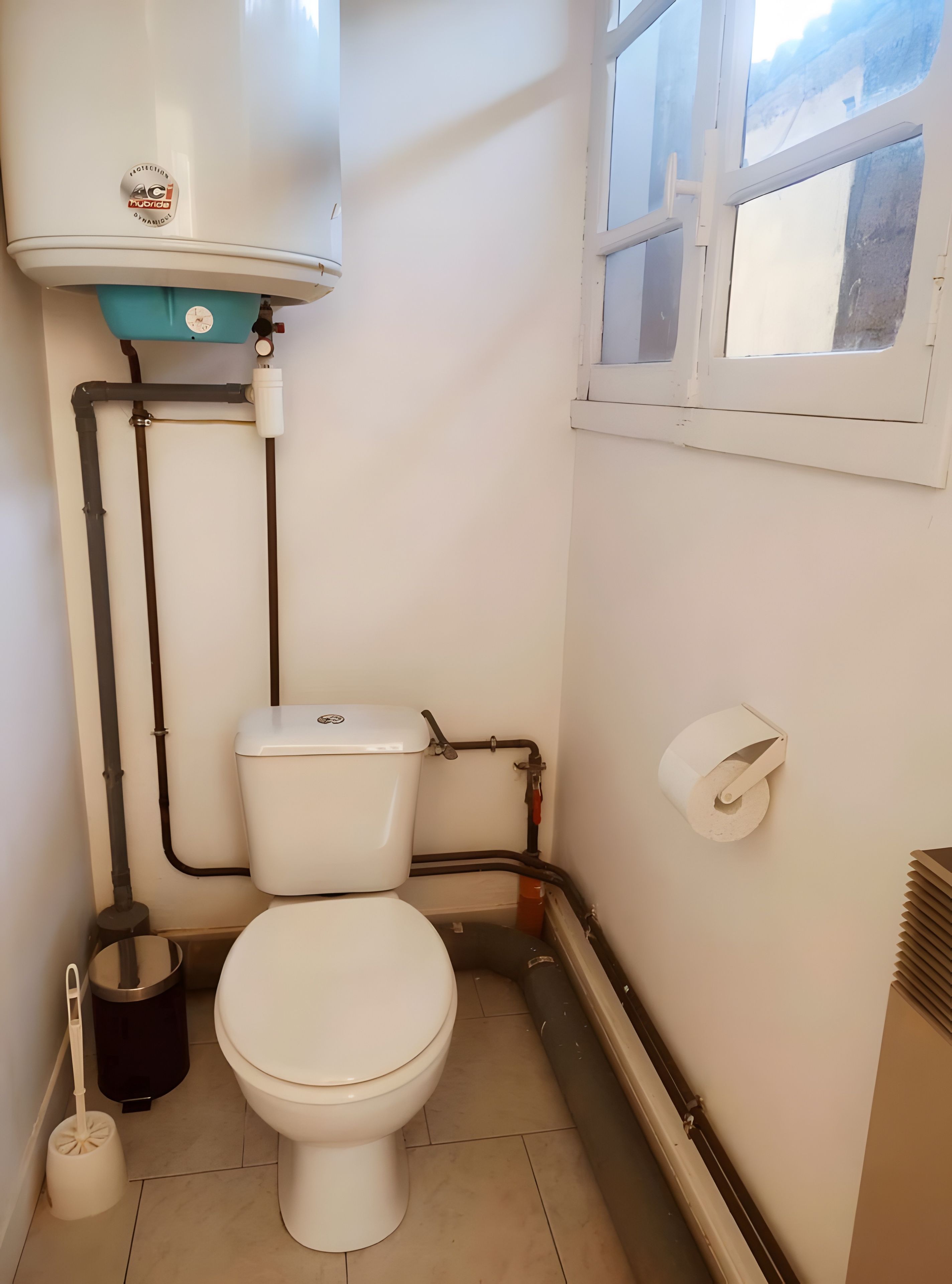Un baño pequeño con inodoro, bidé, cubo de basura y ventana.