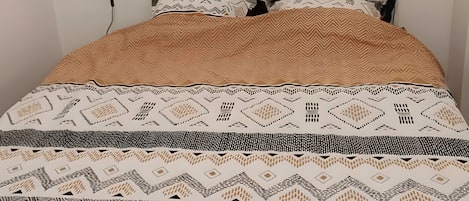 Ein Bett mit gemusterten Betttextilien, zwei Wandlautsprecher und eine Wanddekoration.