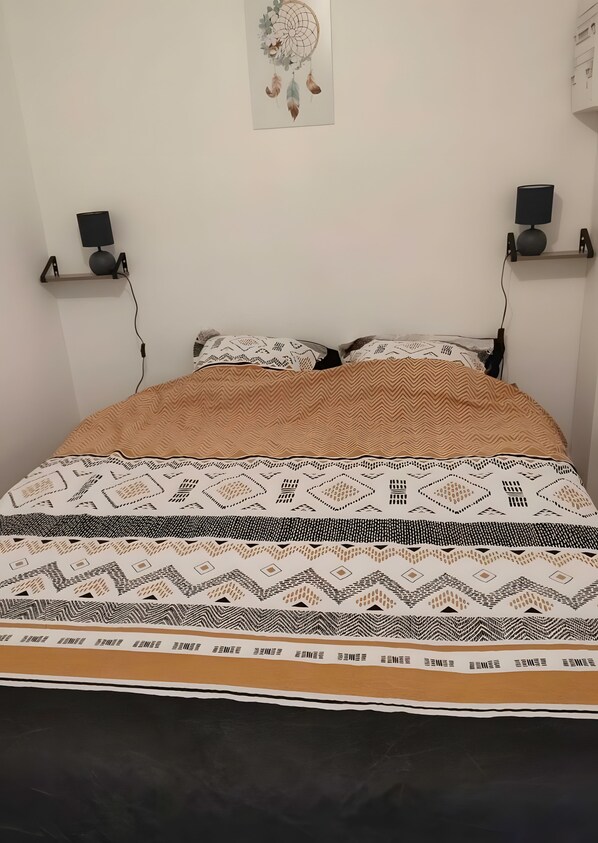 Un letto con lenzuola decorate, due altoparlanti a parete e un addobbo murale.