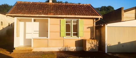 Une maison de plain-pied avec un toit en tuiles, une porte d’entrée et une fenêtre avec des volets.