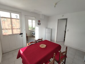 Un'area pranzo con un tavolo rosso, sedie di legno, un frigorifero e una porta che dà su un'altra stanza.