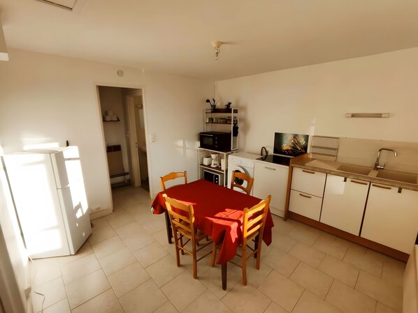 A compact kitchen with a dining table, chairs, a refrigerator, a microwave, and a washing machine.