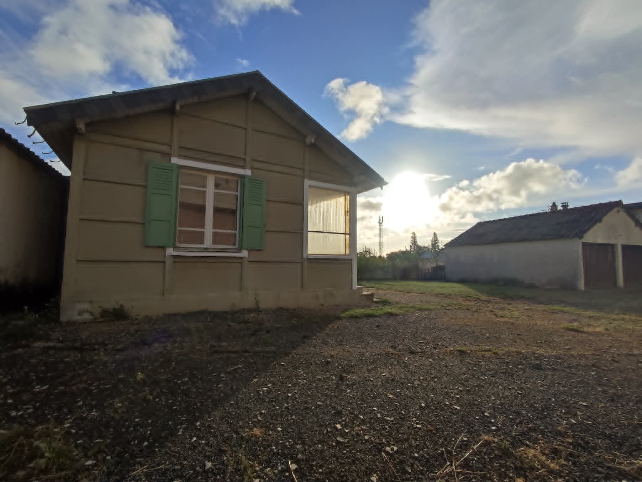 Une maison de plain-pied avec un toit en pente, une fenêtre à l’avant avec des volets et une allée gravillonnée.