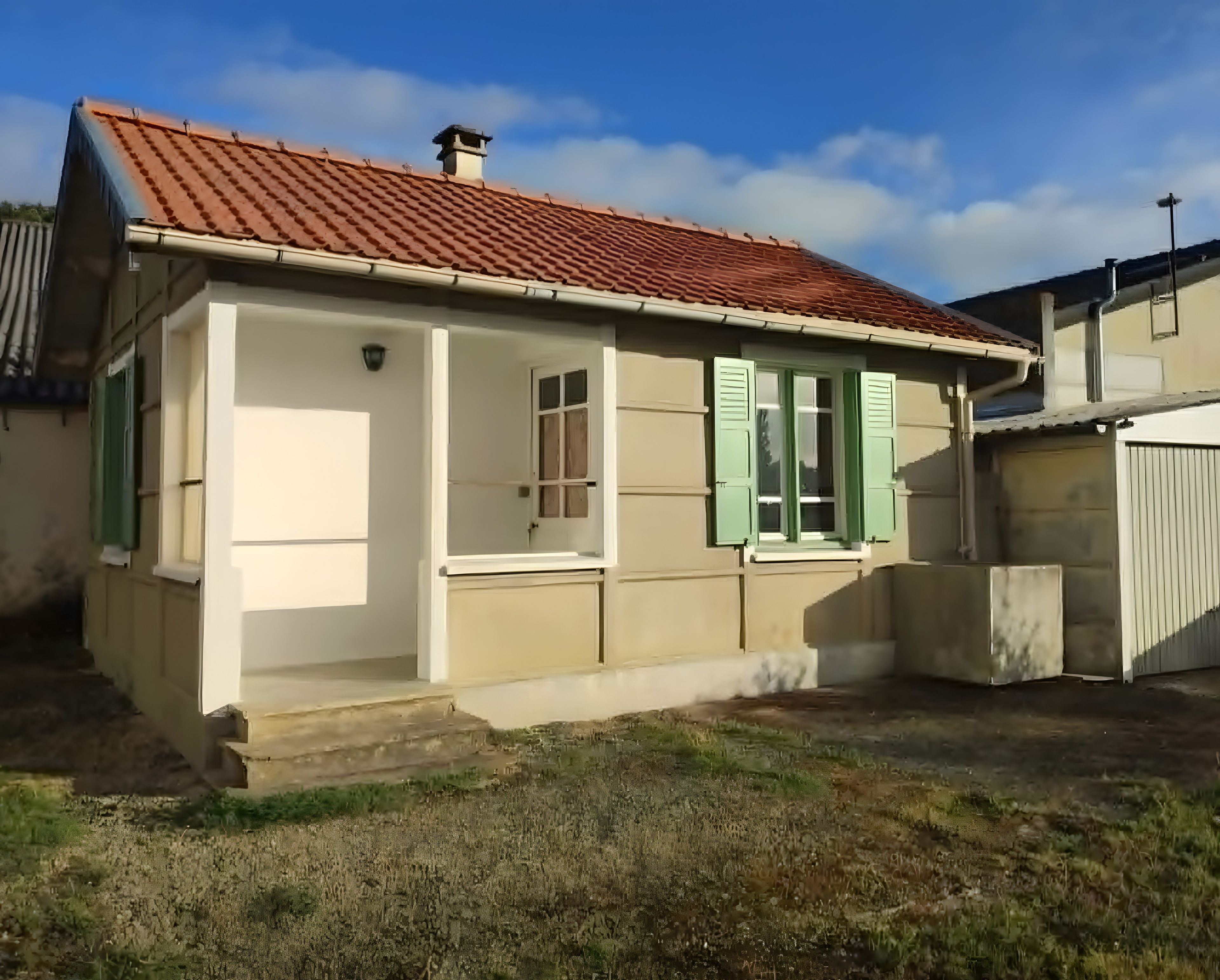 Ein eingeschossiges Haus mit rotem Ziegeldach, einer Veranda und einem kleinen Garten.