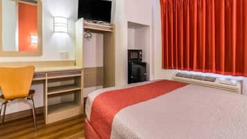 A hotel room with a bed, a desk, a chair, a television, a coffee machine, and a window with curtains.