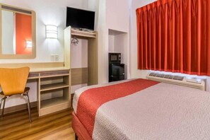 Quarto de hotel com cama, escrivaninha, cadeira, televisão, máquina de café e janela com cortinas.