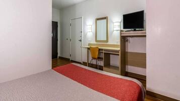 Een hotelkamer met een bed, een bureau, een stoel, een televisie en een spiegel.