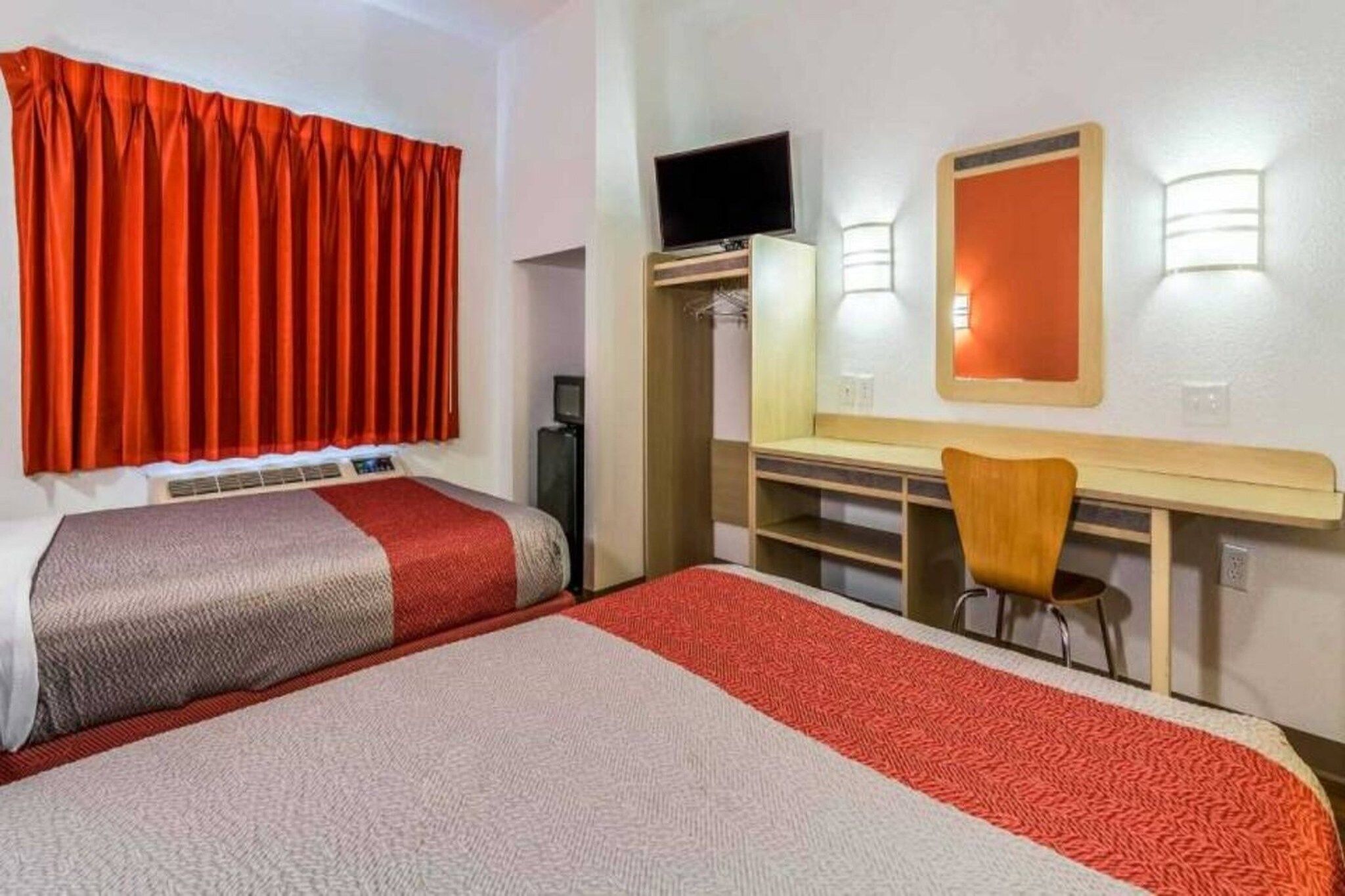 A hotel room with a bed, a desk with a chair, a television, and a wardrobe.