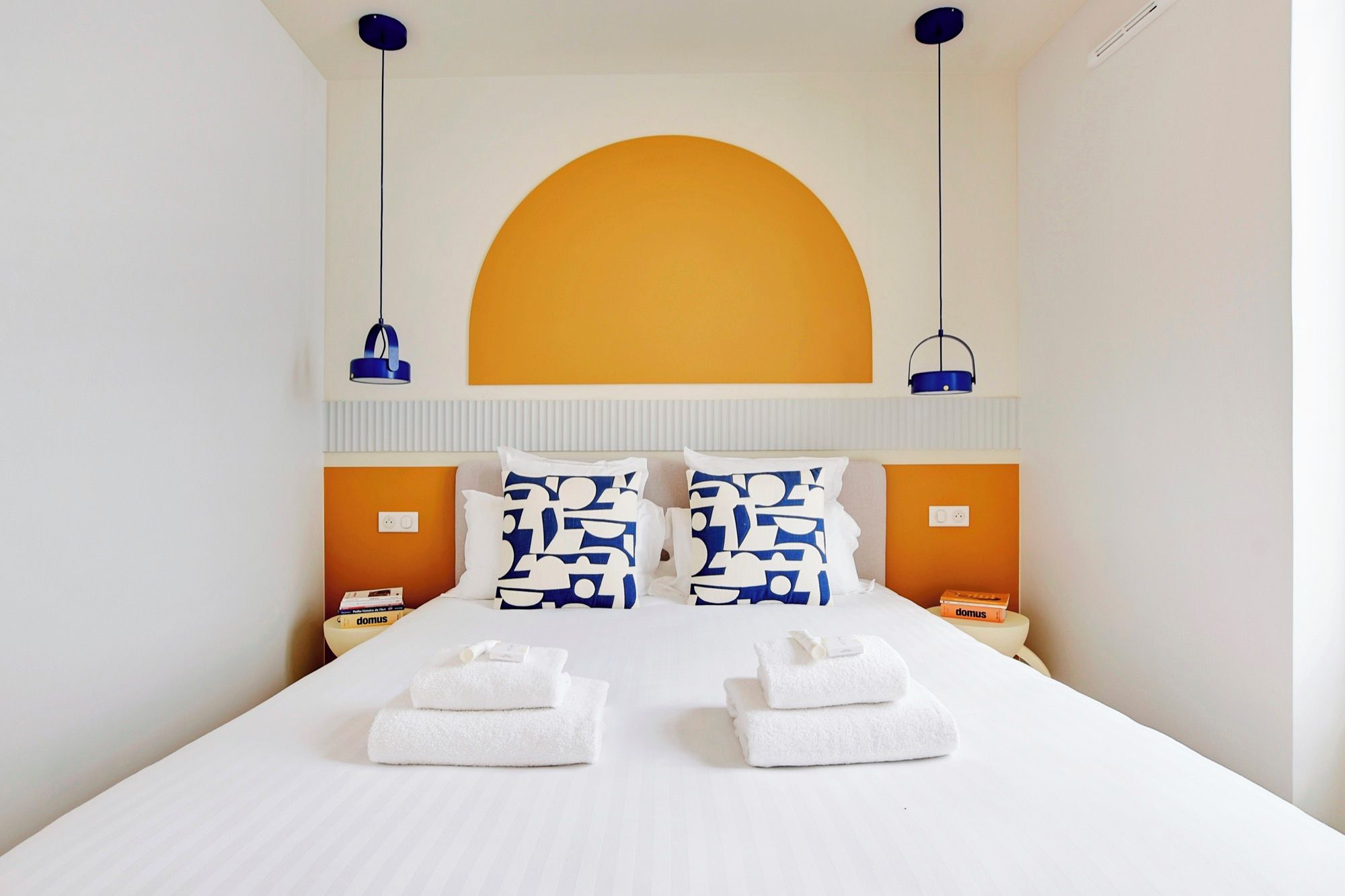 Ein Hotelzimmer mit einem großen Bett, zwei Nachttischen, einer Wandleuchte zum Lesen und einem großen Fenster.