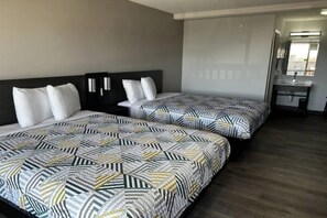 Camera d'albergo con due letti, una testiera scura, un comodino e un bagno con lavandino e specchio.