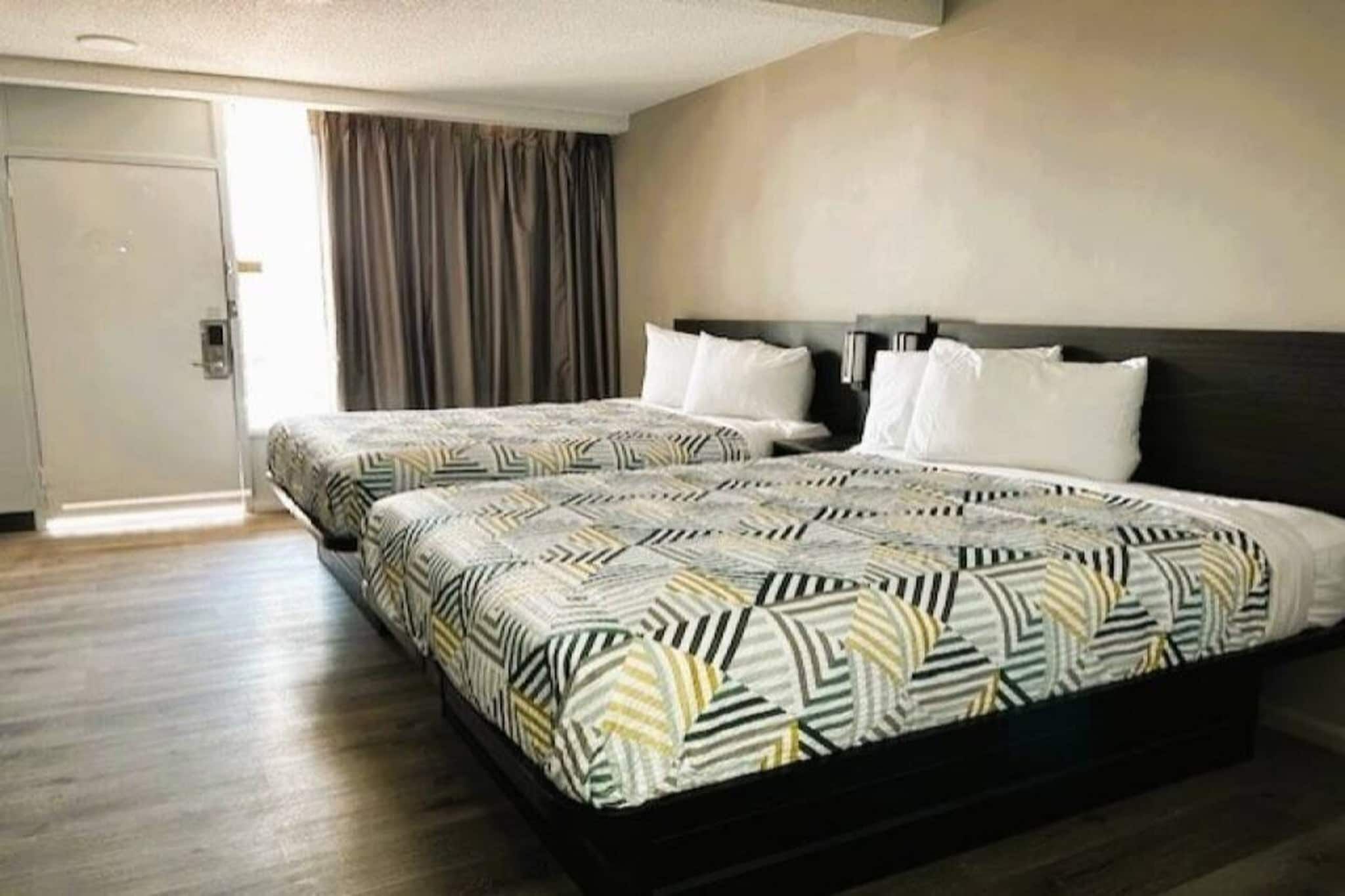 A hotel room with two beds, a wooden floor, a door, and a curtain.