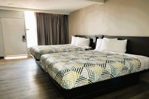 A hotel room with two beds, a wooden floor, a door, and a curtain.